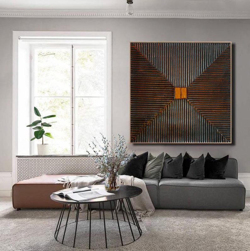 May include: A square abstract painting with a geometric design of intersecting lines in shades of brown, gray, and orange. The painting is hanging on a wall in a living room setting.