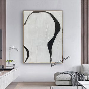 May include: Abstract painting with a white textured background and bold black curved lines. The artwork is framed in a gold-colored frame and hangs on a white wall. The text "Abstract Maker" is visible in the lower right corner.