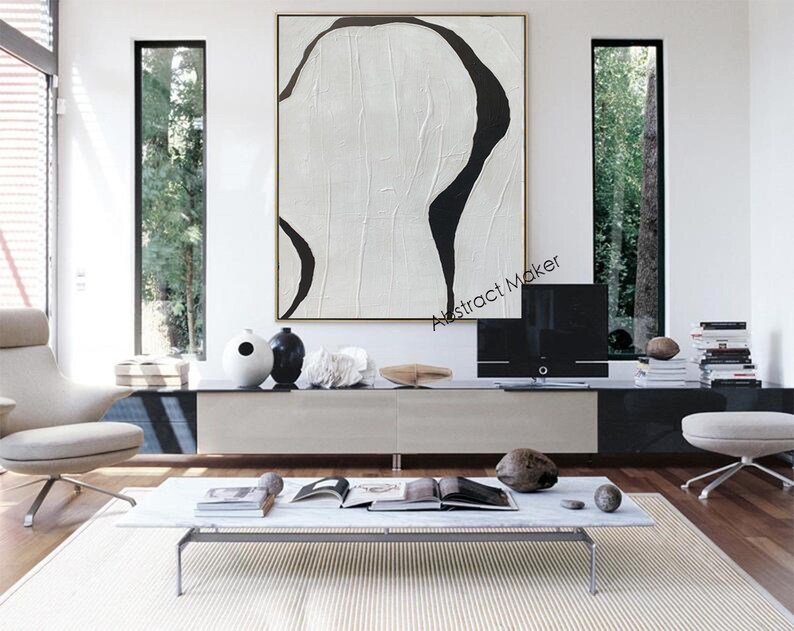 May include: Large abstract painting with a white textured background and bold black curved lines. The artwork is displayed in a modern living room setting, above a low cabinet. The room features minimalist furniture and decor.