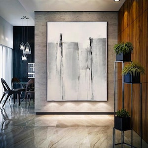 May include: Abstract painting with vertical gray and white brushstrokes on a white canvas. The painting is hanging on a wall in a modern home.