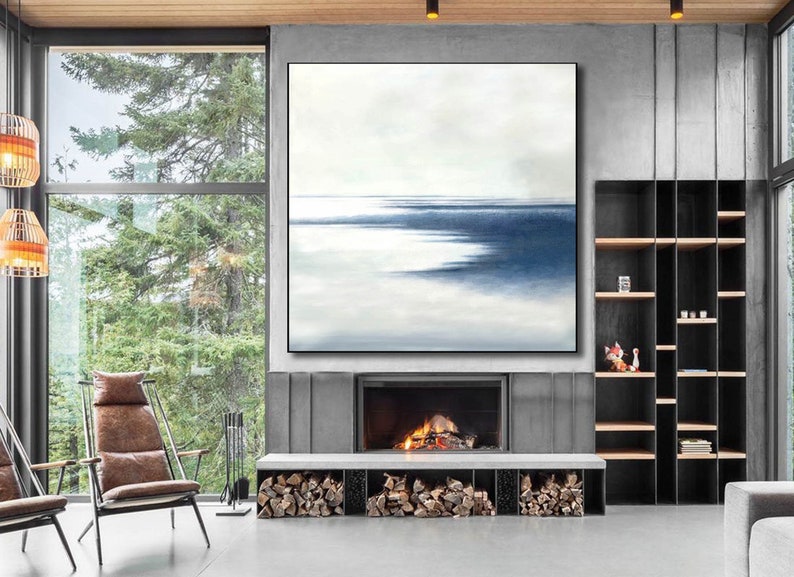 May include: Large abstract painting with a minimalist design. The artwork features a serene landscape with a gradient of white and blue hues, framed in a black border. The painting hangs above a fireplace, enhancing the room's modern aesthetic.