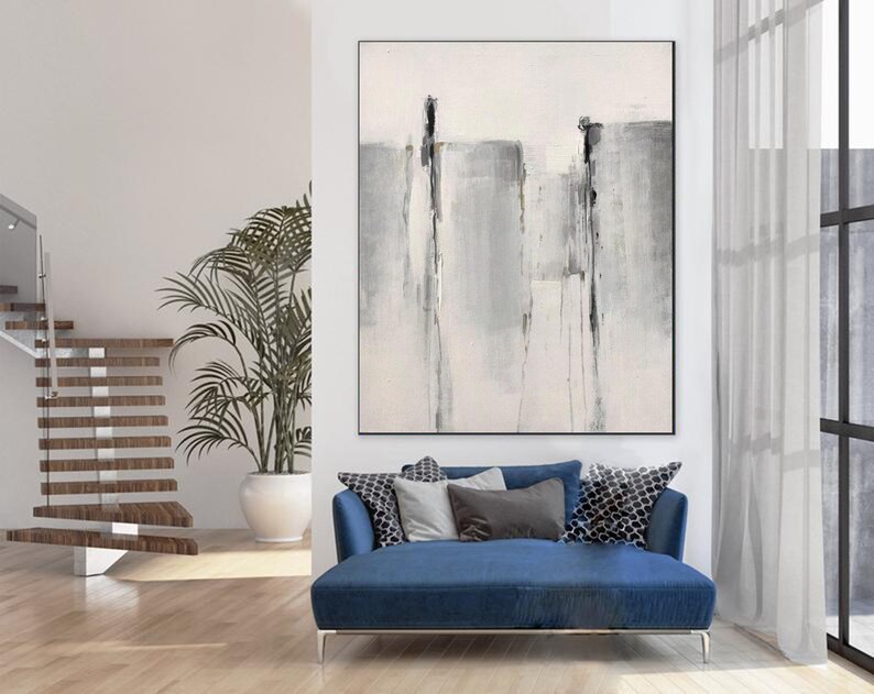 May include: Abstract painting in shades of gray and white with black lines. The painting is hanging on a white wall in a modern living room with a blue sofa and a potted plant.