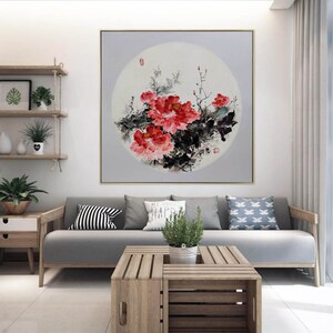 Puede incluir: Una gran pintura cuadrada enmarcada con un dise&ntilde;o floral. La obra de arte muestra vibrantes peon&iacute;as rojas con follaje negro y verde sobre un fondo gris suave. La pintura se exhibe en un sal&oacute;n moderno.