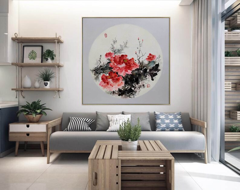 Puede incluir: Una gran pintura cuadrada enmarcada con un dise&ntilde;o floral. La obra de arte muestra vibrantes peon&iacute;as rojas con follaje negro y verde sobre un fondo gris suave. La pintura se exhibe en un sal&oacute;n moderno.