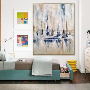 May include: An abstract painting in a gold frame, featuring vertical brushstrokes in white, blue, and brown. The artwork hangs above a bed with a teal frame and a gray comforter. Two framed collages and a yellow side table are also visible.