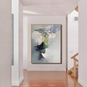 May include: Abstract painting with shades of green, blue, and white. The painting is framed and hanging on a white wall in a hallway.