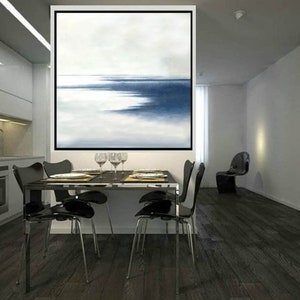 May include: An abstract painting with a black frame depicts a seascape in shades of blue and white. The artwork hangs above a dining table set with plates, glasses, and four black chairs. The room has dark wood flooring and a modern aesthetic.