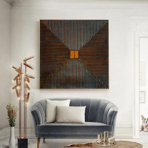May include: A square abstract painting with a geometric design of dark brown and orange stripes. The painting is hanging on a white wall above a gray sofa.