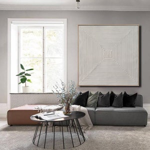 May include: A gray sectional sofa with plush velvet cushions and a white abstract painting above it. The sofa is in a living room with a coffee table and a window in the background.