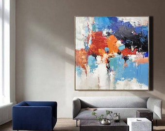 Puede incluir: Pintura abstracta con trazos audaces de pintura azul, naranja, roja y negra sobre un lienzo blanco. La pintura está enmarcada y colgada en una pared en un salón.