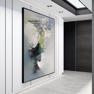 May include: Abstract painting in shades of green, white, and black on a canvas. The painting is framed in a black frame and is hanging on a white wall.