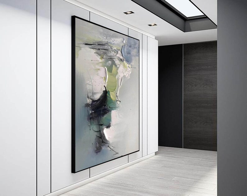 May include: Abstract painting in shades of green, white, and black on a canvas. The painting is framed in a black frame and is hanging on a white wall.