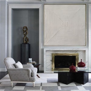 May include: A living room with a gray armchair, a black coffee table, and a fireplace with a white marble surround. A large white abstract artwork hangs above the fireplace.