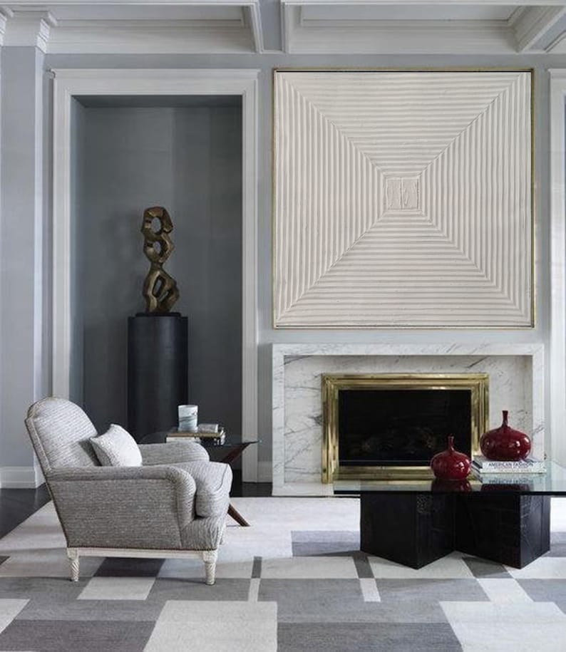 May include: A living room with a gray armchair, a black coffee table, and a fireplace with a white marble surround. A large white abstract artwork hangs above the fireplace.