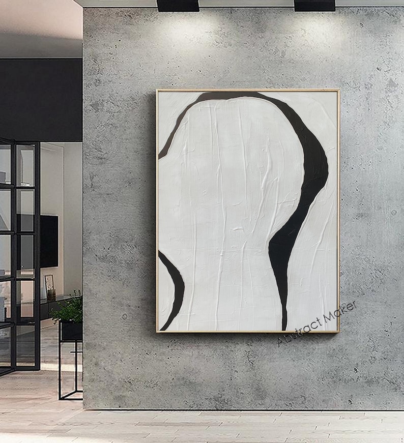 May include: Abstract art piece featuring a black, organic shape against a white background. The artwork is framed in a gold-colored border and mounted on a gray wall. The painting has a textured appearance, with visible brushstrokes. The artwork is minimalist in style, with a focus on form and contrast.