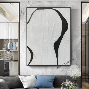 May include: Abstract art piece with a textured white background and bold black curved lines. The artwork is framed in a black rectangular frame and hangs on a marble-patterned wall. The text "Abstract Maker" is visible in the lower right corner.
