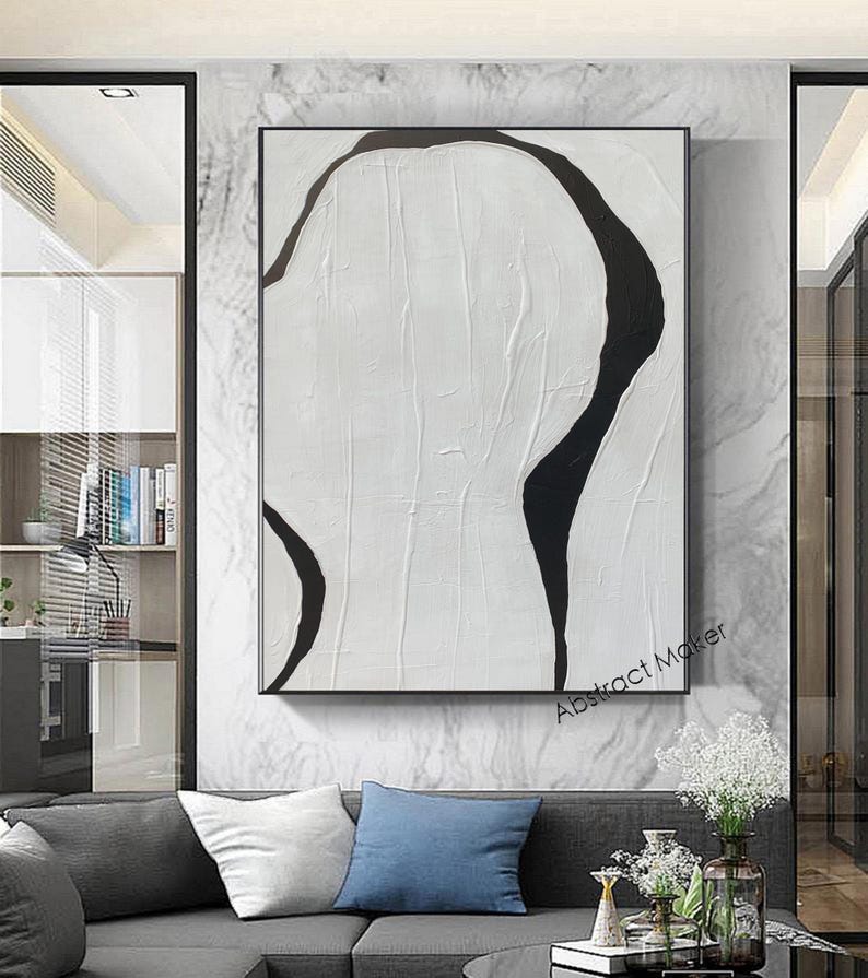 May include: Abstract art piece with a textured white background and bold black curved lines. The artwork is framed in a black rectangular frame and hangs on a marble-patterned wall. The text "Abstract Maker" is visible in the lower right corner.