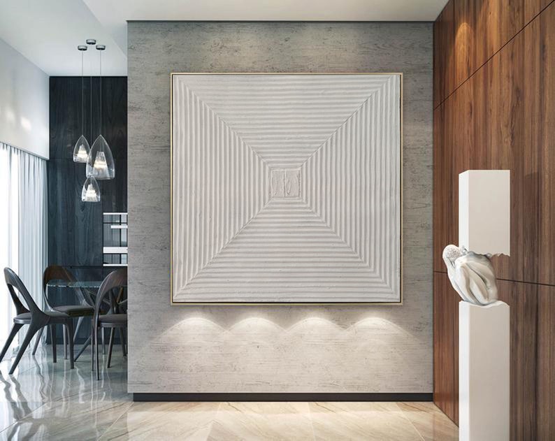 May include: A white textured abstract painting with a geometric design in a gold frame hanging on a gray wall in a modern home.