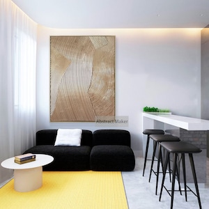 Puede incluir: Un dise&ntilde;o de interior de sala de estar con un sof&aacute; seccional negro, una mesa de caf&eacute; blanca, una alfombra amarilla y una gran pintura abstracta con l&iacute;neas doradas y marrones. La pintura est&aacute; colgada en una pared blanca. Hay tres taburetes de bar negros en el fondo.