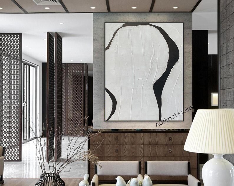 May include: Large abstract painting with a black and white design. The artwork features a textured white background with bold, curved black shapes. The painting is framed and displayed in a modern interior setting.
