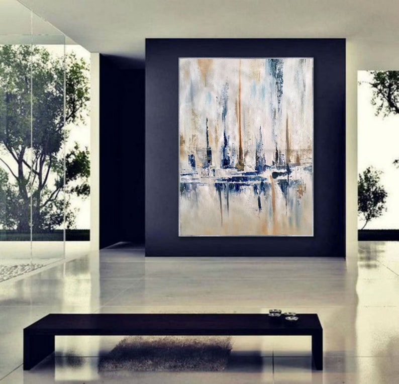 May include: Abstract oil painting on canvas featuring a coastal scene with vertical brushstrokes in white, blue, and tan. The artwork is displayed in a modern, minimalist interior with a dark accent wall and a black bench.