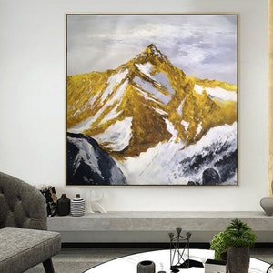 May include: A painting of a mountain range with a golden peak and white snow. The sky is a light blue with white clouds. The painting is framed in a gold frame.