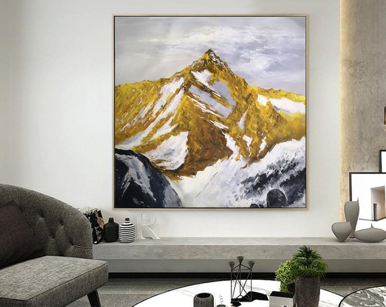 May include: A painting of a mountain range with a golden peak and white snow. The sky is a light blue with white clouds. The painting is framed in a gold frame.