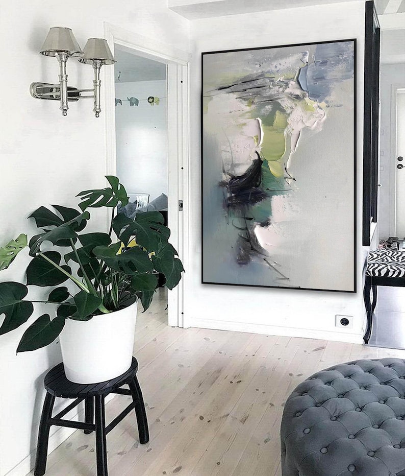 May include: Abstract painting in shades of green, white, and gray with black accents. The painting is framed in a black frame and hangs on a white wall in a hallway.