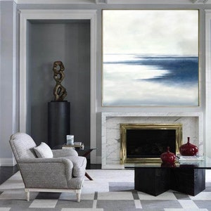 May include: An interior living room scene featuring a large abstract painting with blue and white hues above a fireplace. A gray armchair, a black coffee table, and a geometric patterned rug complete the space. Decorative red vases sit on the table.