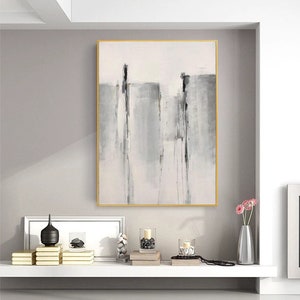 May include: A framed abstract painting with a white background and gray and black brushstrokes. The painting is hanging on a wall above a shelf with decorative objects.