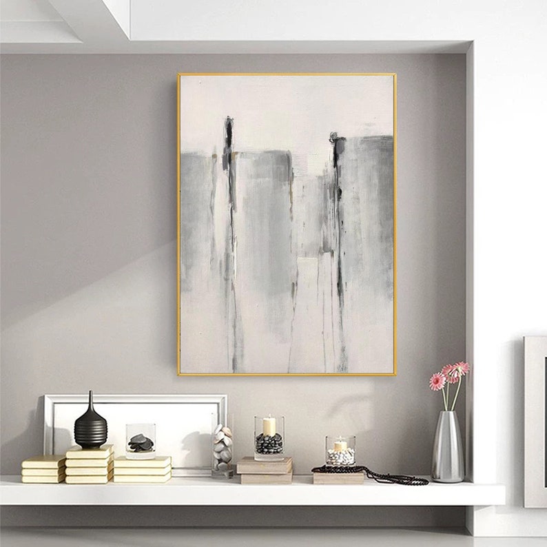May include: A framed abstract painting with a white background and gray and black brushstrokes. The painting is hanging on a wall above a shelf with decorative objects.