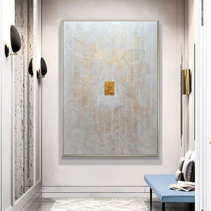 May include: A large rectangular wall art piece featuring a textured white surface with intricate, wavy, embossed lines and subtle gold accents. A small, solid, rectangular gold-leaf panel is positioned directly in the centre of the canvas.