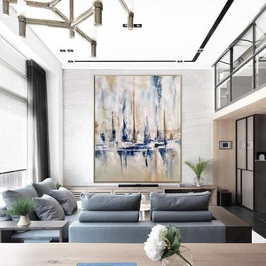 May include: Large abstract painting with vertical brushstrokes in shades of blue, beige, and white. The artwork is displayed in a modern living room with gray sofas, a wooden coffee table, and a decorative chandelier.
