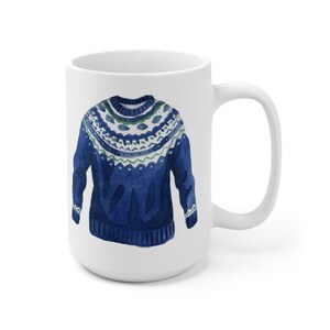 May include: White ceramic mug with a blue and green watercolor illustration of a knitted sweater.