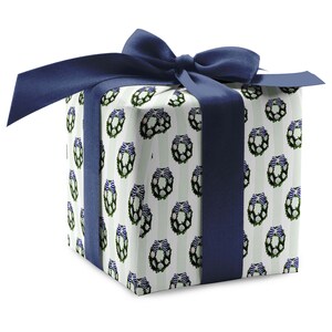 May include: A white gift box with a green and white wreath pattern and a navy blue ribbon.