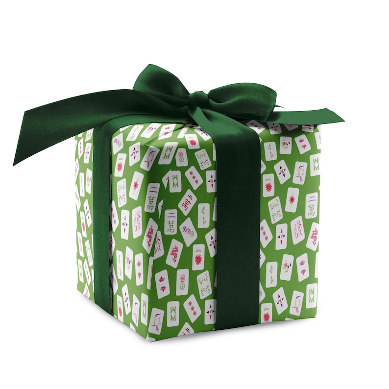 May include: A square gift box wrapped in green paper with a pattern of white and red playing card illustrations. The box is tied with a dark green satin ribbon and bow, creating a festive presentation.