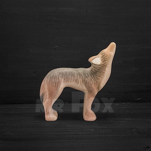 May include: A wooden wolf figurine with a light brown and grey painted finish. The wolf is standing on all four legs with its head tilted back and mouth open, as if howling.