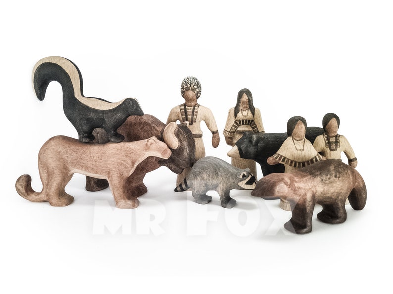 May include: Wooden toy set featuring a skunk, cougar, bison, raccoon, bear, and Native American figures. The animals are in various shades of brown and gray, while the people are in tan and cream colors. The skunk is black and white.