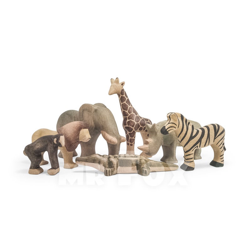 May include: A set of wooden animal figurines, including a giraffe, zebra, rhino, elephant, lion, and monkey, with a crocodile figurine in the center.