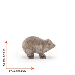 May include: A wooden toy animal, a brown bear, standing on a white surface. The bear is 4.2 cm tall and 6.7 cm long.