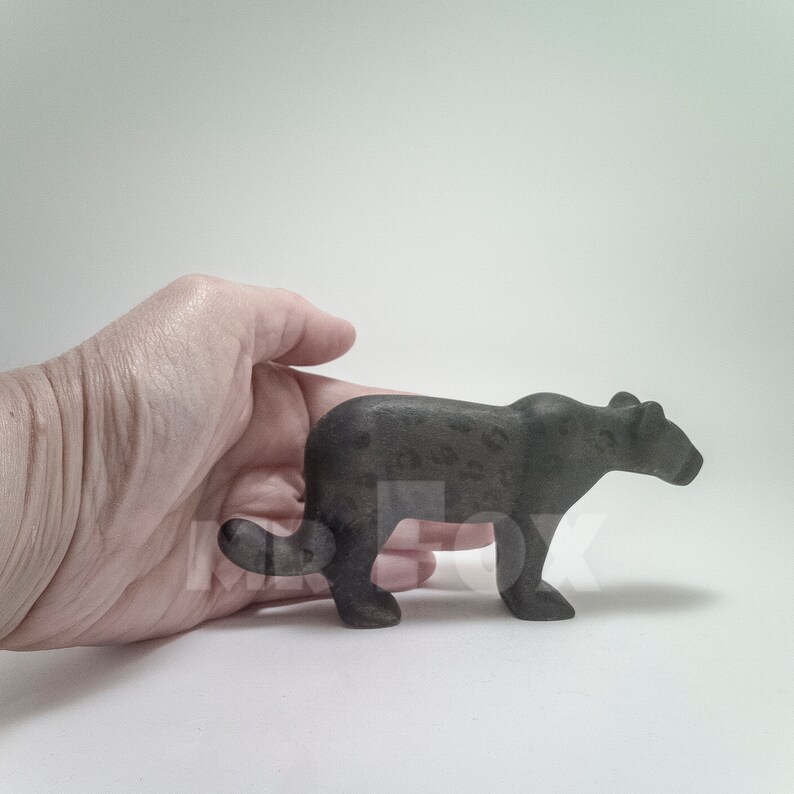 Op de afbeelding: Een zwart houten panterbeeldje met een gevlekt patroon. Het beeldje staat op een wit oppervlak.