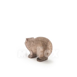 May include: A wooden carved bear figurine, standing on a white surface. The bear is brown and has a simple, rounded design.