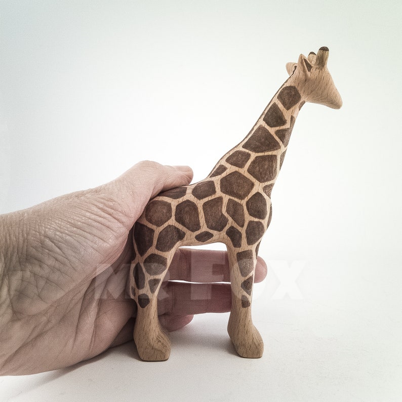 May include: A wooden giraffe figurine with brown and tan paint, standing on a white surface.