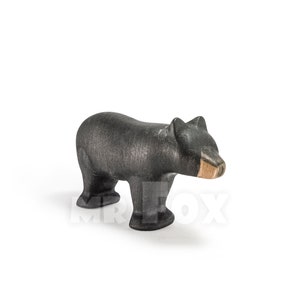 May include: A wooden bear figurine in a standing pose. The bear is primarily black with a natural wood-colored snout. The handcrafted toy has a textured surface and is set against a white background.