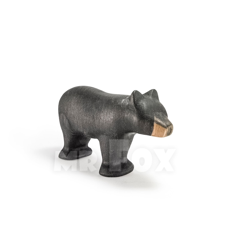 May include: A wooden bear figurine in a standing pose. The bear is primarily black with a natural wood-colored snout. The handcrafted toy has a textured surface and is set against a white background.