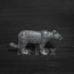 Op de afbeelding: Een grijs, steenachtig beeldje van een panter of luipaard met een gevlekt patroon. Het beeldje staat op een zwarte ondergrond.