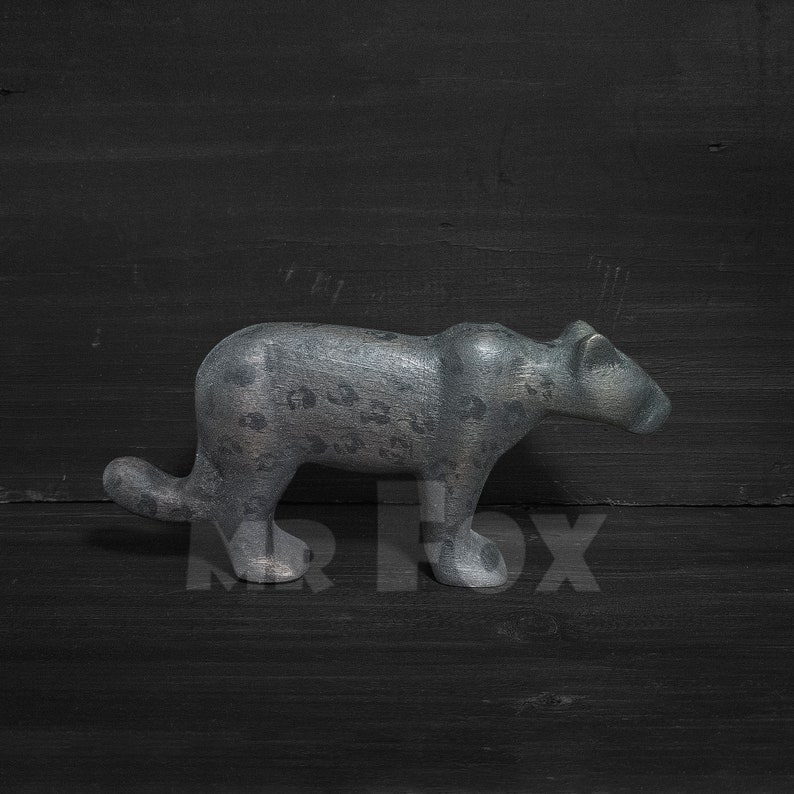 Op de afbeelding: Een grijs, steenachtig beeldje van een panter of luipaard met een gevlekt patroon. Het beeldje staat op een zwarte ondergrond.