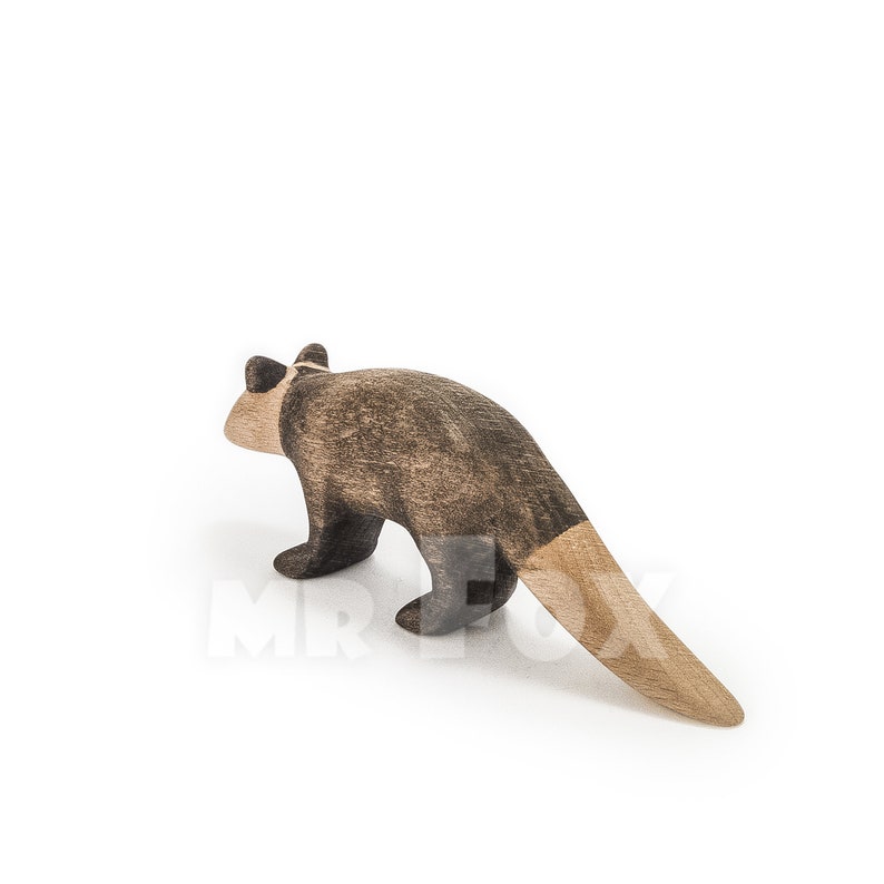 May include: A wooden toy possum figurine. The possum is primarily brown with a lighter brown tail. The toy is made of wood and has a simple, stylized design. The figurine is standing on all fours.