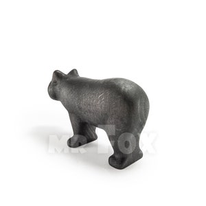 May include: A dark gray bear figurine, viewed from the rear, stands on all fours. The bear has a textured surface and a stylized design. The figurine is set against a white background.