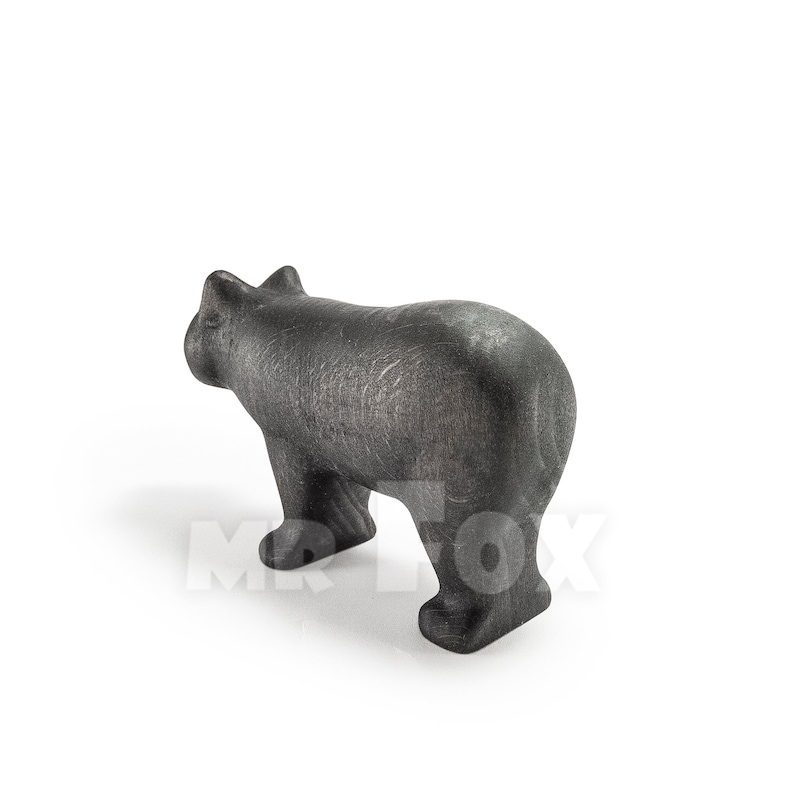 May include: A dark gray bear figurine, viewed from the rear, stands on all fours. The bear has a textured surface and a stylized design. The figurine is set against a white background.